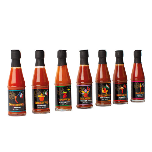 A row of seven small glass bottles from the Chilli Traveller Hot Sauce set, each with a unique, colourful label.