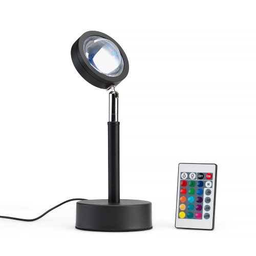 The black Sundown Mood Lamp with an adjustable head, standing next to its multi-coloured remote control on a white surface.