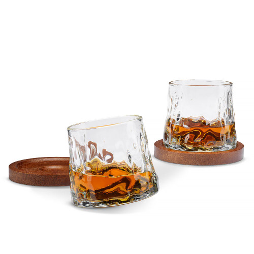 Two whiskey glasses with dark wood coasters. One glass stands upright, while the other is tilted, showing its rotating base.
