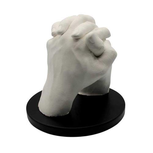 A detailed white cast from a hand moulding kit showing two hands clasped together, mounted on a circular black display stand.