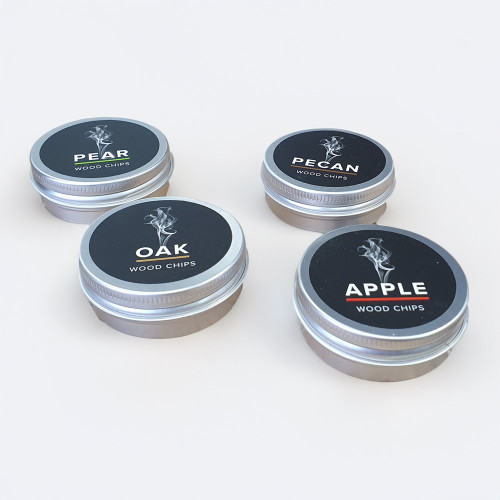 Four small, silver-coloured tins of smoking wood chips for the Whiskey Smoker, showing Oak, Apple, Pear, and Pecan varieties.