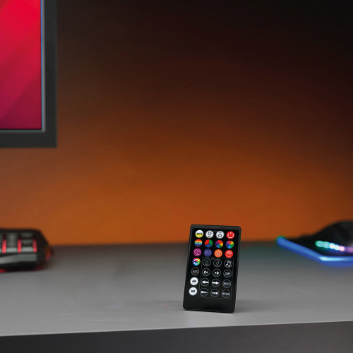 The remote for the RED5 LED Strip Light stands on a grey desk, part of a gaming setup with an orange glow.