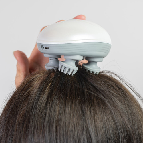 A person using the white and grey rechargeable head massager, its silicone bristles moving through their dark brown hair.
