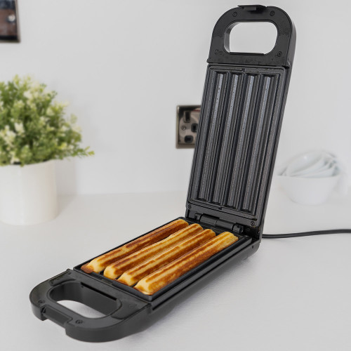 The black Churro Maker is open on a white kitchen worktop, with four golden-brown churros freshly cooked inside.
