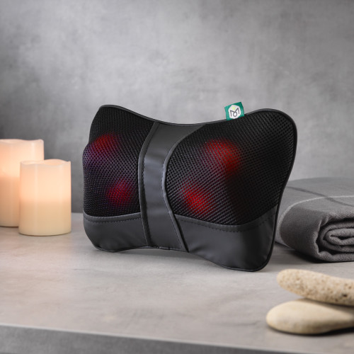 The Wellbeing Mini Massage Cushion sits on a grey surface, its heated red nodes glowing through the black mesh.