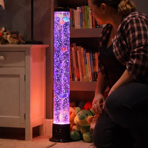 The tall Bubble Fish Tower glows purple in a child's bedroom. A woman kneels beside it, mesmerised by it.