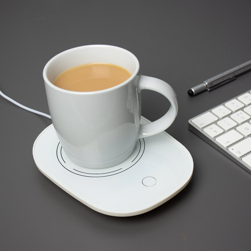 A white USB Cup Warmer keeps a mug of tea warm on a dark grey desk next to a computer keyboard.