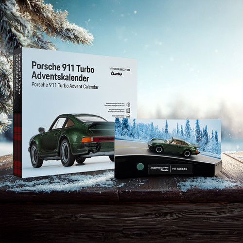 Porsche 911 Turbo Advent Calendar box and completed green model car on a snowy wooden table with a winter forest background.