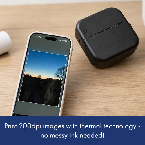 A black thermal phone printer sits on a wooden desk. A smartphone shows a sunset photo, ready for ink-free thermal printing.