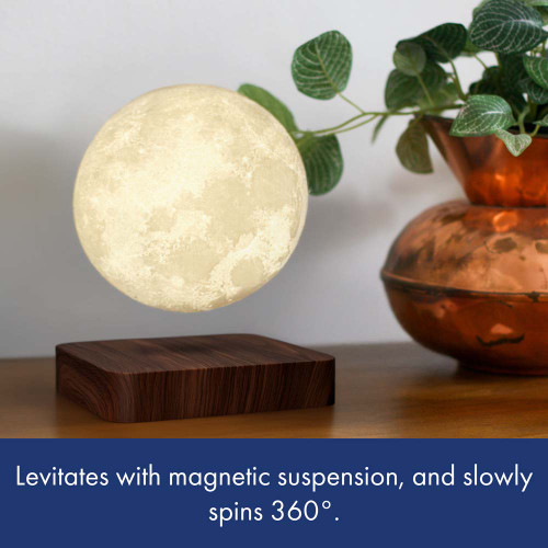 A glowing moon lamp levitates and slowly spins above its dark wood base on a desk, next to a plant in a copper pot.