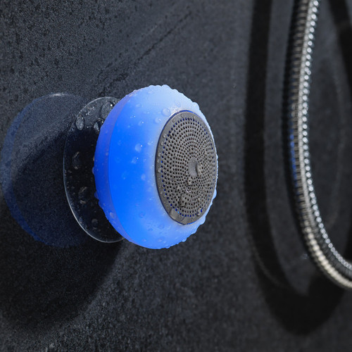 A blue-glowing Light Up Shower Speaker covered in water drops, attached to a dark slate shower wall with its suction cup.