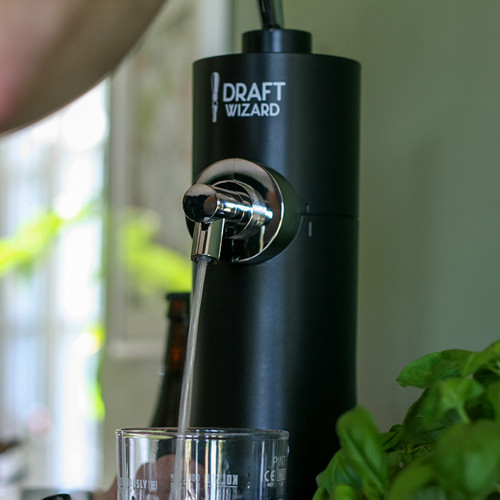 A close-up of the black Draft Wizard beer dispenser pouring from its chrome tap into a pint glass in a home kitchen.