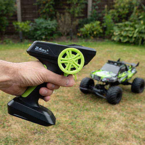 A hand holds the 2.4GHz RC controller for the Rock Monster truck, which sits on a grassy lawn in the background.