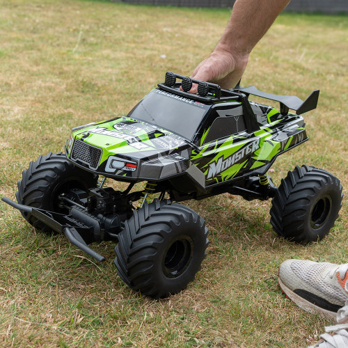 A person's hand places the green and black Rock Monster RC truck with its large tyres onto a lawn.