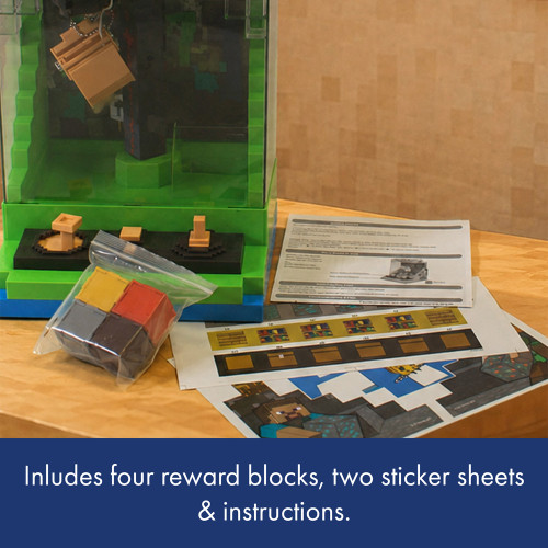 The Minecraft claw crane displayed on a table with its included colourful reward blocks, sticker sheets, and instruction manual.