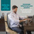A man uses the Shiatsu Massage Cushion on a chair at his home office desk, which folds for easy storage and fits any chair.