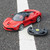 A red La Ferrari remote control car with its steering wheel controller, parked on a tarmac road over a white painted line.
