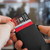 A person sliding a red credit card from a black C-Secure wallet, showing other cards fanned out for easy access.
