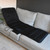 The black Wellbeing Full Body Massage Mat with Heat is unfolded on top a light grey sofa.