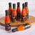 Seven small bottles of Chilli Traveller hot sauce on a round wooden board. One bottle lies on its side in the foreground.