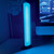 A sound reactive light bar stands on a desk, glowing bright cyan next to a monitor displaying a video game.