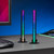 Two sound reactive light bars glowing with a colourful gradient, standing on a grey desk next to a keyboard and monitor.