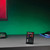 The black remote for the LED strip light on a grey desk in a gaming setup, with a wall glowing green in the background.