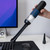 A person holds the blue and black portable mini vacuum, using the brush attachment to clean a computer keyboard.