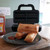Three fresh sausage rolls on a plate with ketchup. The open Sausage Roll Maker is on the kitchen counter.