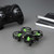 A small black-and-green Nano Drone V2 quadcopter sits on a gray surface next to a black game controller, a black notebook, and a pen.