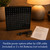 A black square Word Clock on a desk, displayed with its USB cable, instruction manual, and three AA batteries for power.