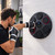 A circular black speaker boxing pad mounted on a wall outside with the arm of a man punching, wearing the gloves.