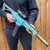 A person holds the light blue and grey Rapid Fire foam dart shooter with a scope, long magazine, and silencer.