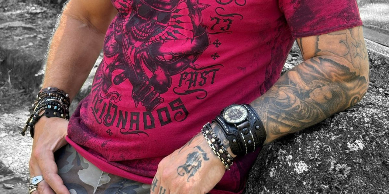 Man wearing a black leather cuff watch with stacked leather bracelets, styled with a red graphic t-shirt and tattoos.