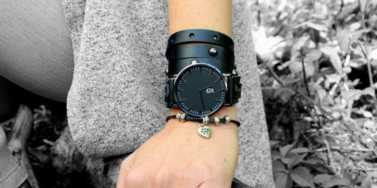 Bracelet watch for women featuring a black leather cuff strap with studs, styled with a silver heart charm bracelet.