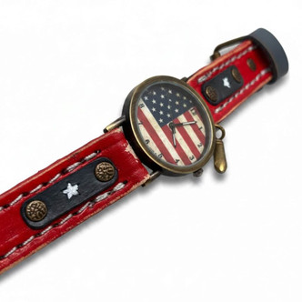 Close-up of American flag quartz watch with distressed red full-grain leather, navy blue star accents, contrasting stitching, and vintage brass-tone hardware.