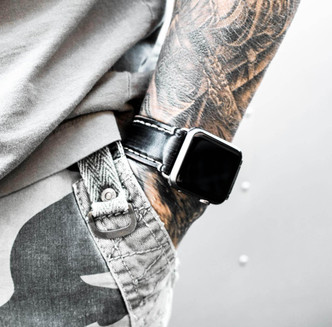 Tattooed model wearing distressed black leather Apple Watch strap, styled with contrast stitching and bold streetwear.