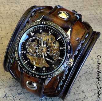 Close-up of handmade leather cuff watch showing detailed stitching and riveted design on aged brown leather band. Close-up of handmade leather cuff watch showing detailed stitching and riveted design on aged brown leather band.