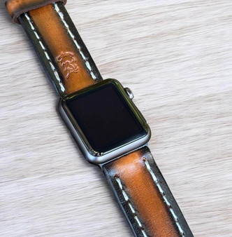 Unisex brown leather Apple Watch band with visible black edges and white contrast stitching.