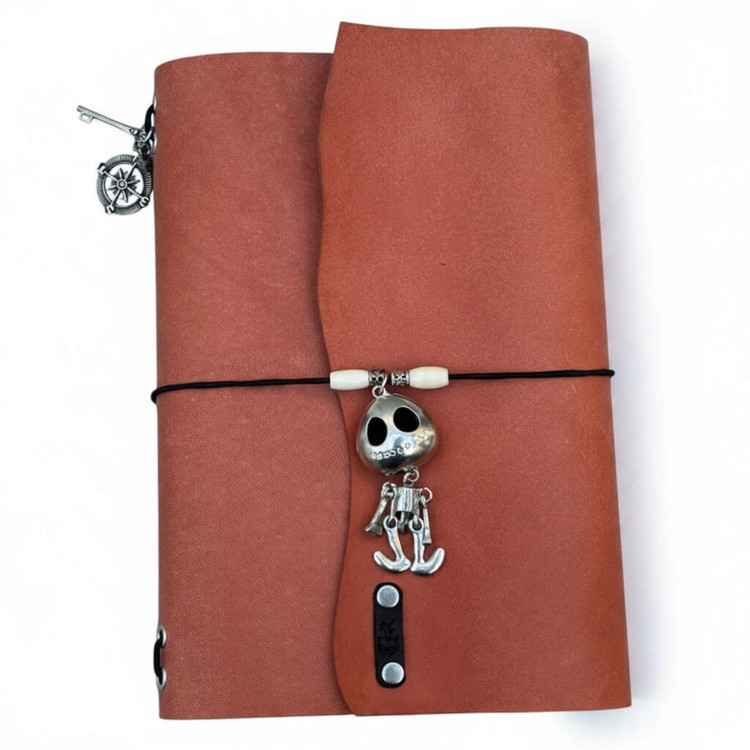 Handmade burnt orange A5 leather journal with skeleton charm, ivory-colored beads, curved flap, and decorative metal accents.