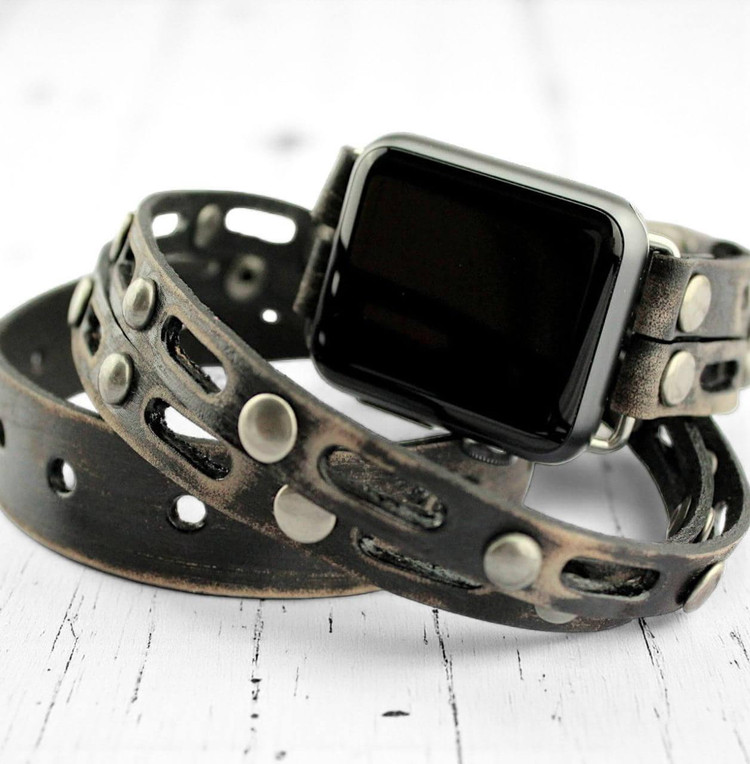 Apple Watch wrap band for men made from distressed full-grain leather with silver rivets, photographed on white table.