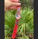 Full-length view of red leather American flag watch held outdoors, showing buckle closure, adjustable strap holes, white stitching, and navy leather details.