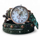 Close-up of green full-grain leather wrap watch with Cuckoo Nest world map dial, copper-tone cross charm, verdigris leaf clock charm, and decorative rivet details.