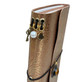 Close-up of metallic gold floral leather journal spine with vintage key, pearl-style bead, and antique brass-tone charms.
