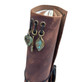 Close-up of distressed brown leather journal spine with antique brass-tone heart and leaf charms, turquoise patina, and metal eyelets.