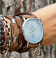 Handmade brown leather wrap watch worn on a woman's wrist, showing layered leather straps, patterned details, and silver-tone accents.