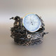 Women's snake skin embossed leather watch showing woven black cord threading, silver eyelets and slim flat watch case, side angle view