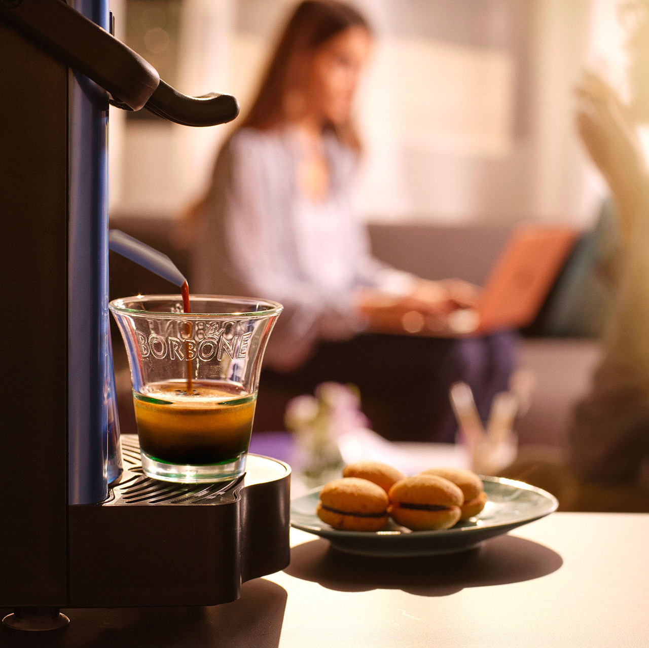 a lifestyle photo of a caffe borbone Didi machine brewing a cup of espresso into a glass cup with macarons on the table a lifestyle photo of a caffe borbone Didi machine brewing a cup of espresso into a glass cup with macarons on the table