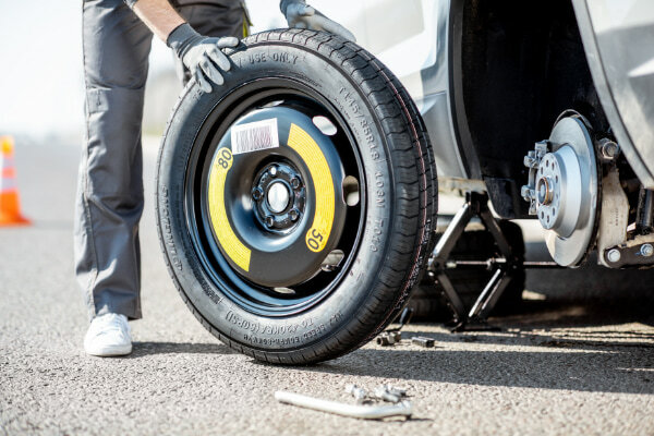 Example of a spare tire being put on a jacked up vehicle with a tire udner vehicle for safety