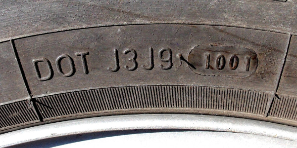 Close-up of a tire sidewall showing a DOT code of 1001, indicating the tire was manufactured in the 10th week of 2001.